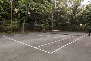 A tennis court surrounded by a fence and trees at The Brittany Apartments, Maryland